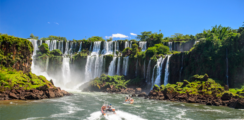 A pair of boats navigating the waters below several waterfalls at the famous Iguazu Falls