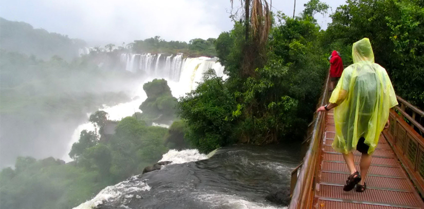 2 Tourists walking across a bridge overlooking the Igazu Falls on the Brazilian side.