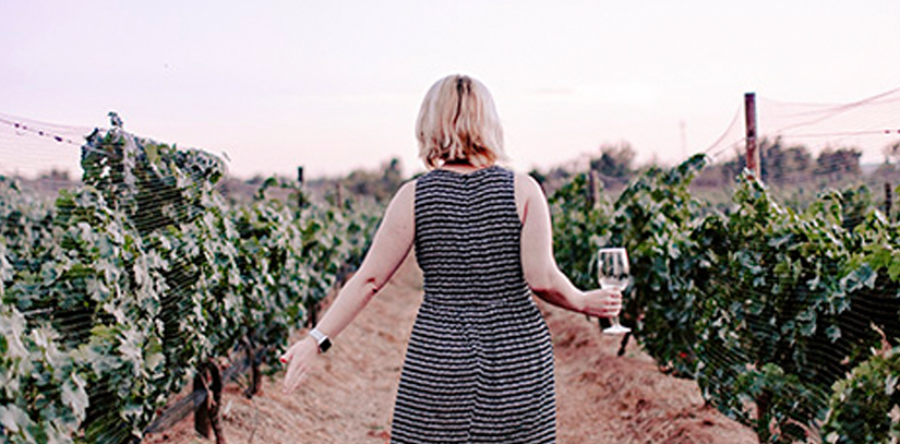 A woman strolling through  a beautiful vineyard holding a glass of wine