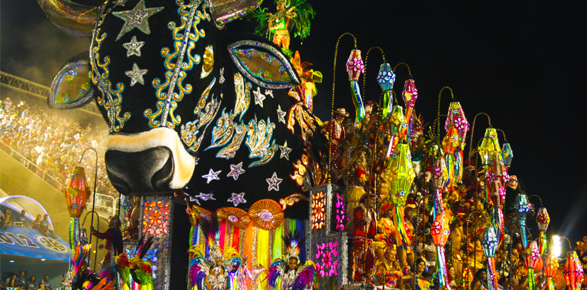 Spectators looking on as dancers dressed in extravagant clothing and stood on a Bull Float perform for carnival in Brazil