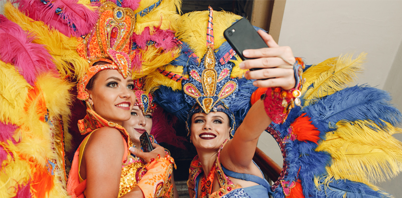 Three Carnival dancers dressed in extravagant clothing smile while taking a selfie