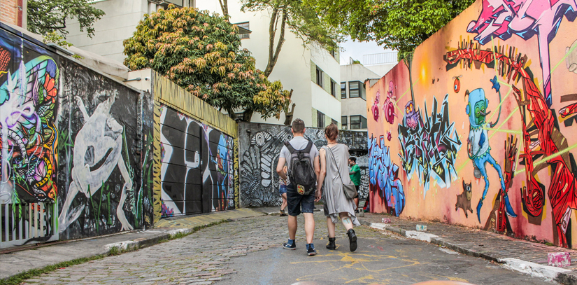 A couple holding hands while walking down an alley filled with street art in Sao Paolo