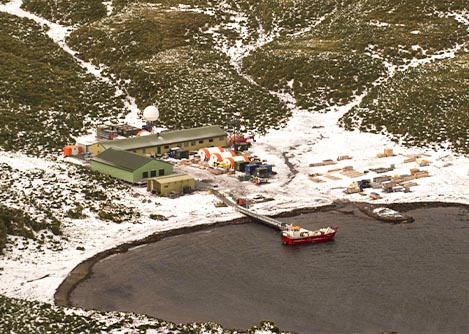 An aerial view of a small research center with a boat docked offshore in Antarctica.
