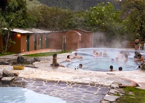 Visitors enjoying a thermal pool in Baños, with a small building and some trees in the background.