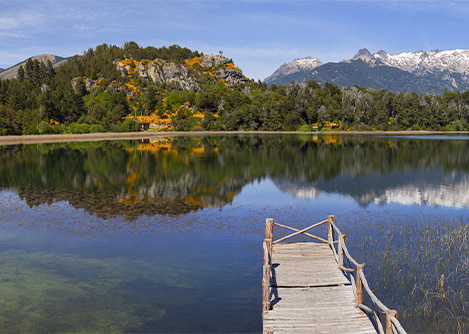 A wooden dock on a lake in Patagonia, with mountains and forested hills visible in the distance.