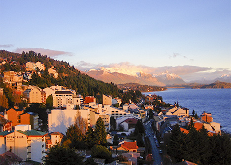 Sunset over the city of Bariloche and Lake Nahuel Huapi with mountains visible in the distance.