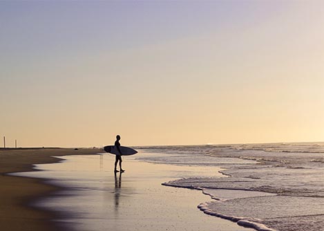 A man carrying a surfboard on the beach in Florianopolis, a popular destination for surfers.