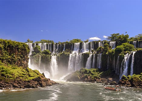 A boat navigating the water below several two-tiered waterfalls, part of the enormous Iguazu Falls.