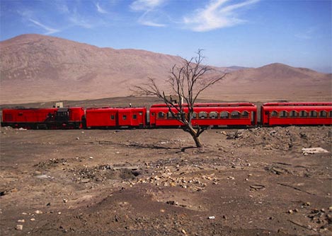 The bright red Trans-Atacama Train traveling through a desolate area in the Atacama Desert.
