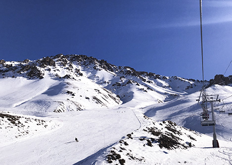 A ski lift and a person skiing down a snow-covered mountainside at the Las Leñas Ski Resort.