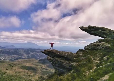 A man posing on a rocky outcrop in front of breathtaking landscapes at Itacolomi State Park.