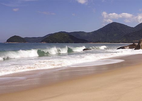 Waves crashing onto a deserted beach with lush, jungle-covered hills visible in the distance.