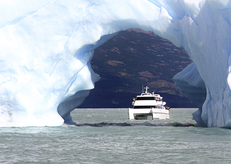 A cruise ship navigating under a natural archway made of ice in Argentine Patagonia.