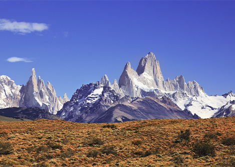 Mount Fitz Roy and other surrounding mountains, overlooking an orange-tinted field.