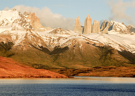 The iconic Torres del Paine overlooking some rugged, snow-covered terrain and a nearby lake.