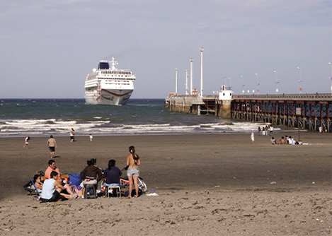 Visitors on the beach next to the pier in Puerto Madryn, with a large cruise ship just offshore.