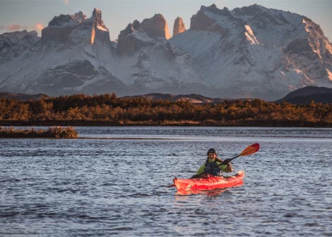 A woman paddling a kayak on the Serrano River, overlooked by beautiful snow-covered mountains.
