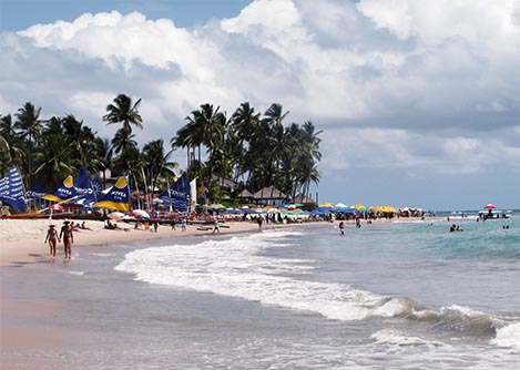 Crowds of visitors at Porto de Galinhas, a sandy beach overlooked by palm trees.