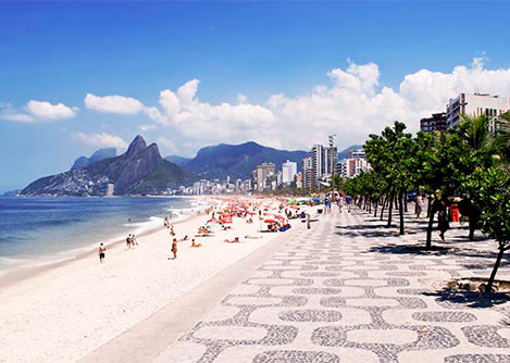 A tree-lined sidewalk next to Copacabana Beach, with Sugarloaf Mountain visible in the distance.