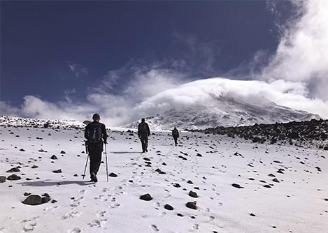 Three hikers walking across a snowy surface on the way to the top of the Chimborazo Volcano.