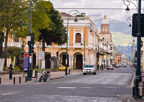 A cobblestone street next to a plaza in Riobamba, with historic buildings in the background.
