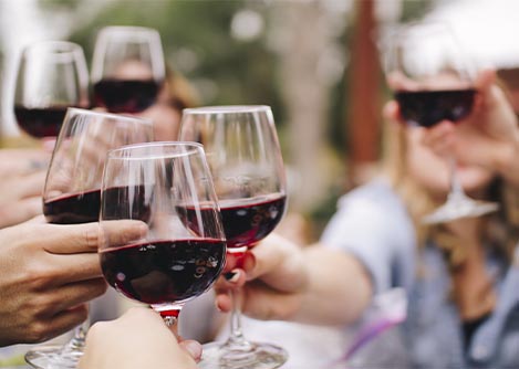 A group of people toasting with wine glasses full of red wine at a wine tasting event.