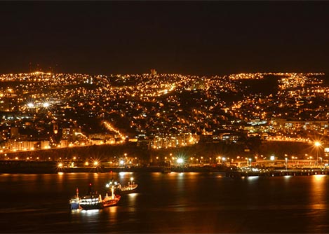 A pair of boats in the Pacific Ocean, overlooked by the sparkling lights of the city of Valparaiso.